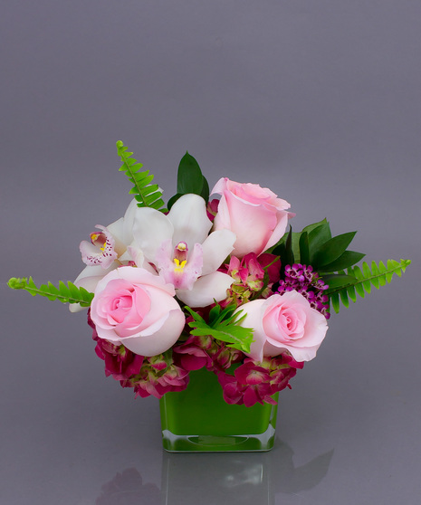 Our Gentle Embrace is a sweet vase designed using fresh roses, orchids, and hydrangea all in a leaf lined cube.  Approximately 8