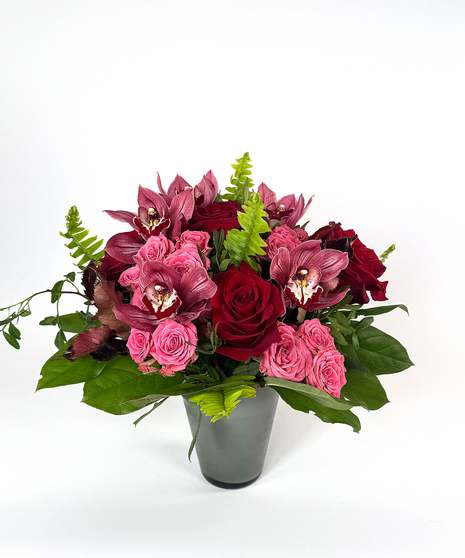 red and pink roses with greenery in a grey container