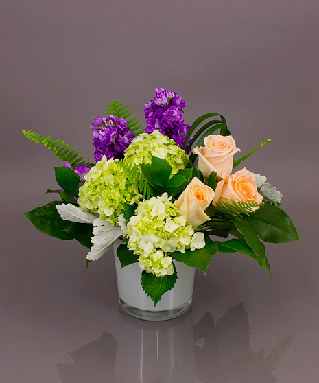 This fun pastel design of pink roses, purple stock and green hydrangeas in a glass cylinder vase is the perfect gift for spring!