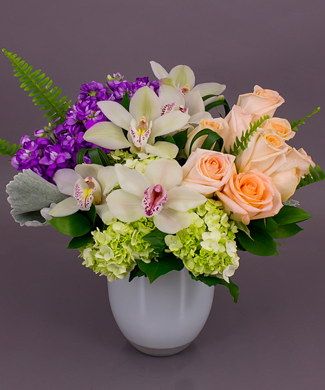 This fun pastel design of pink roses, purple stock and green hydrangeas in a glass cylinder vase is the perfect gift for spring!